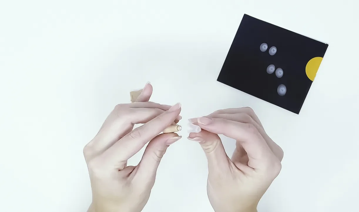 Hands attaching an ear tip to a hearing aid with extra ear tips visible