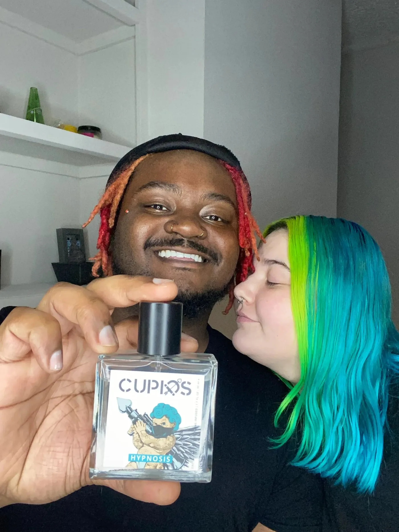 A person holding a bottle of Cupids Hypnosis perfume with a couple in the background