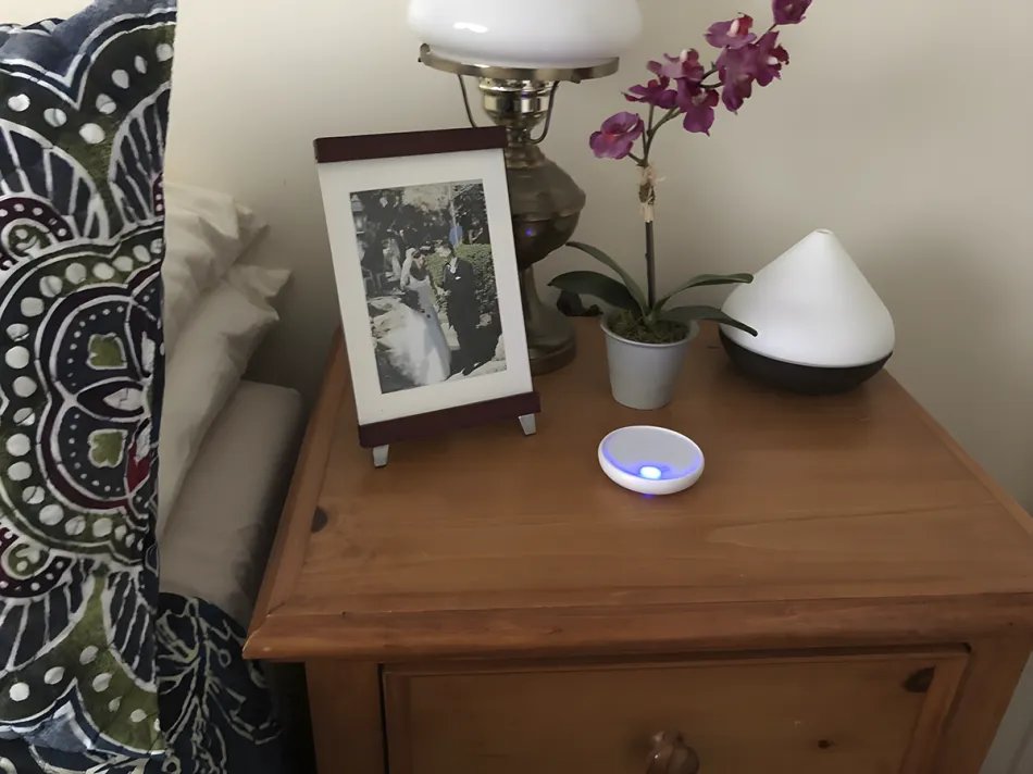 Dodow device sitting on a nightstand next to a bed