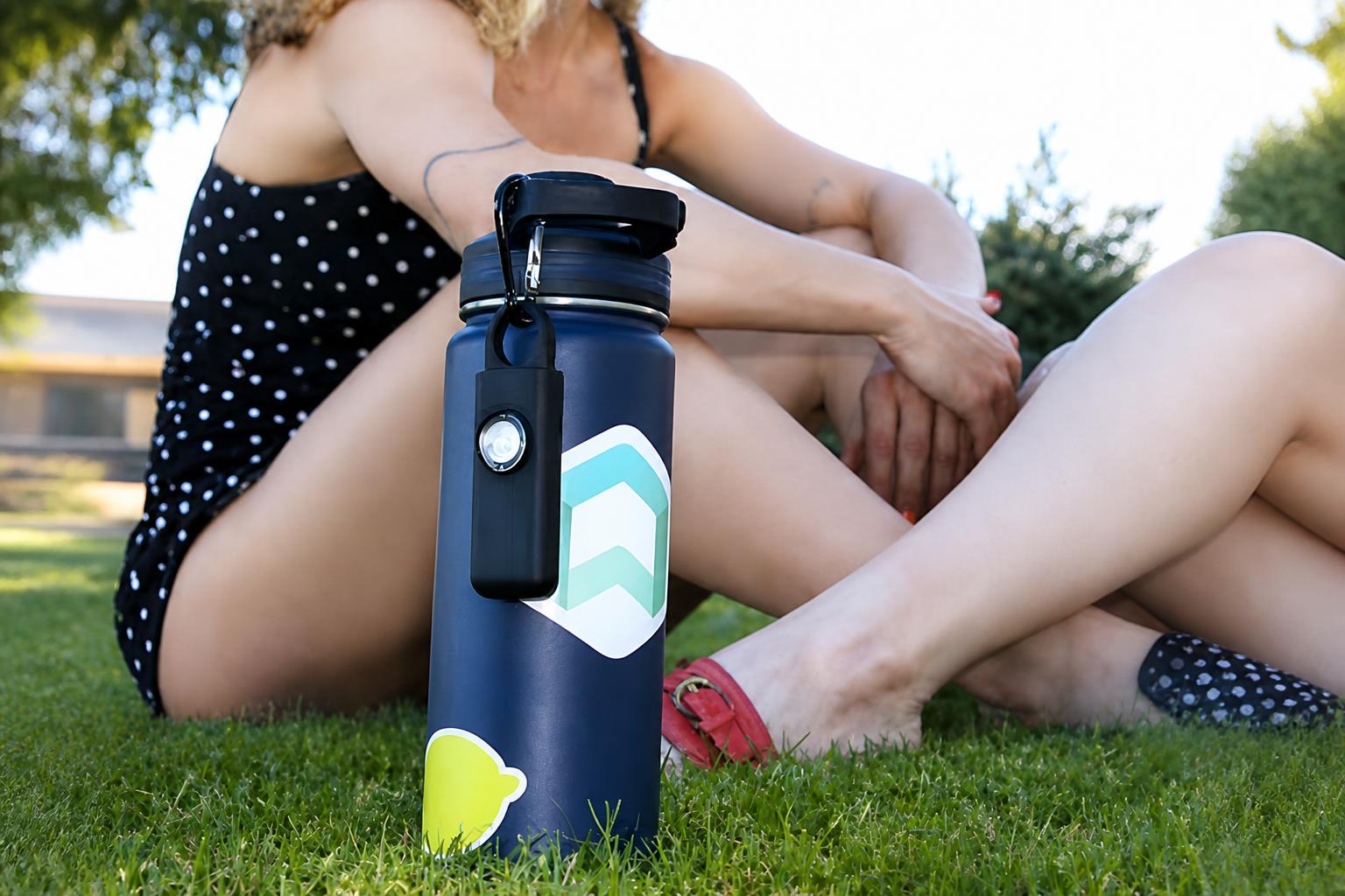 A small clip-on device attached to the side of a reusable water bottle outdoors