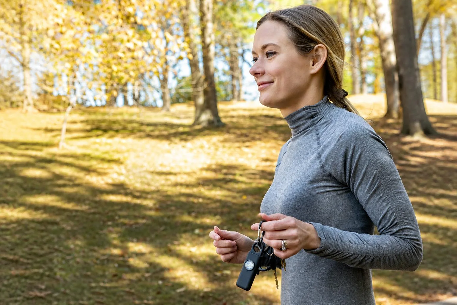 A woman jogging outdoors holding a small mint-green personal alarm alongside her keys