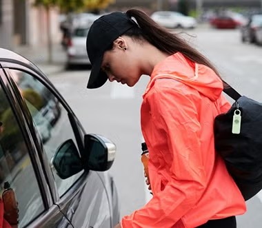A woman in a bright orange jacket getting into her car while holding her keys and phone