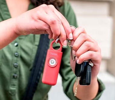 A close-up of a red Hootie alarm with visible branding, held on a keyring next to a set of house keys