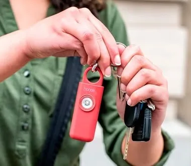 A close-up of a red Hootie alarm with visible branding, held on a keyring next to a set of house keys
