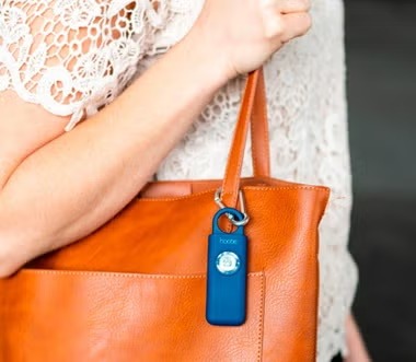 A blue Hootie alarm clipped to a tan tote bag