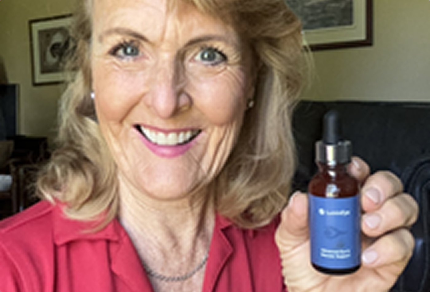 Woman smiling and holding a bottle of LuminEye in a home setting