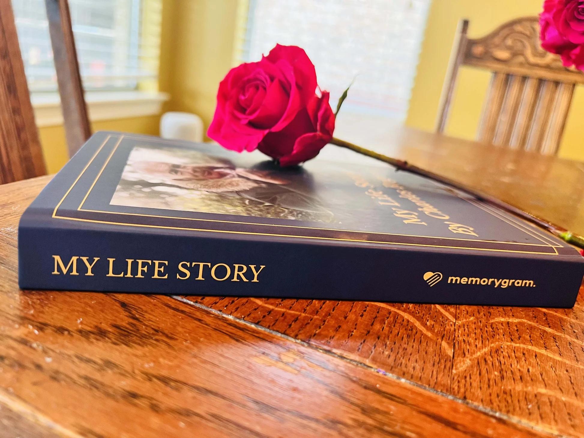 The spine of a personalized memory book titled 'My Life Story' with a rose placed on top