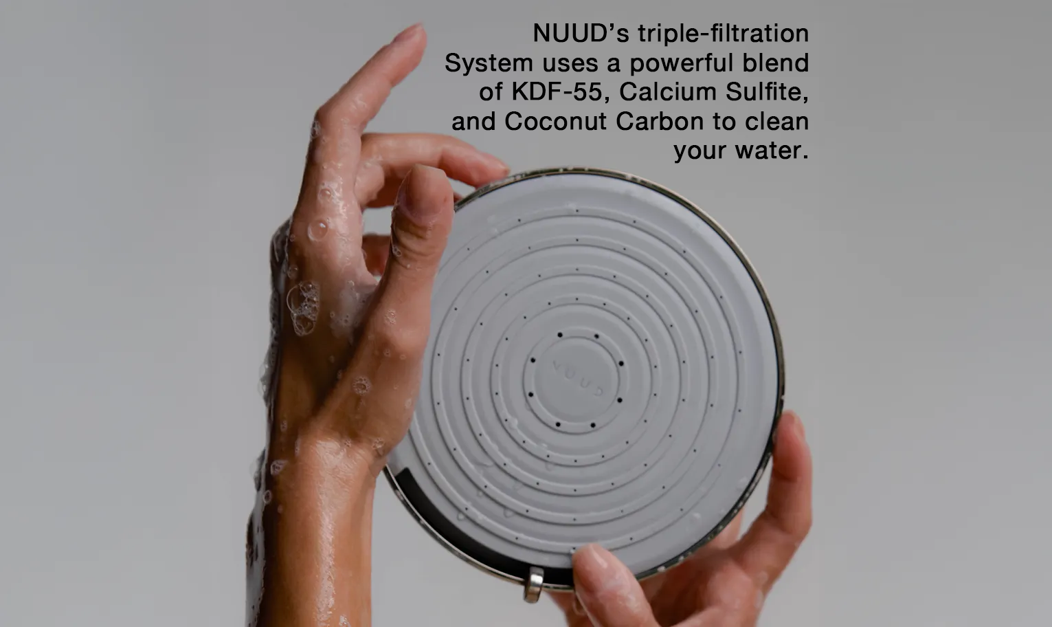 Hands holding NUUD showerhead with triple-filtration system callouts