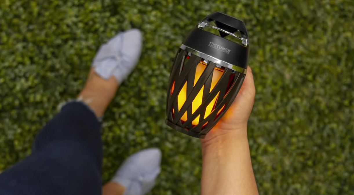 A person holding a TikiTunes speaker while standing on grass