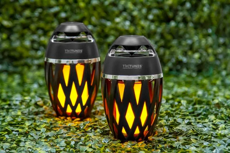 Two TikiTunes wireless speakers with ambient flame lights placed on green foliage
